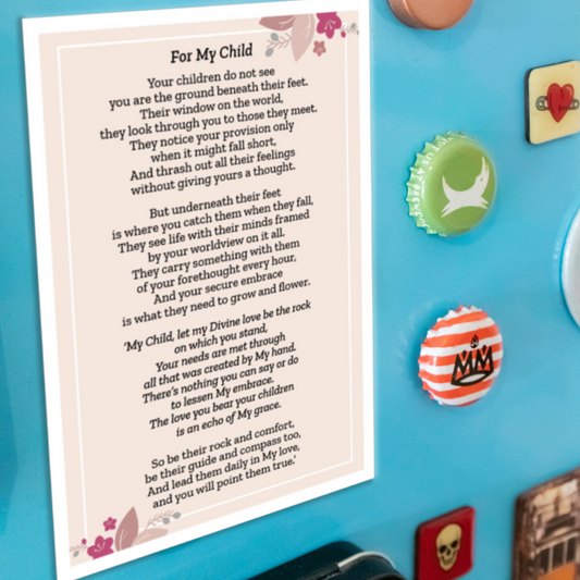A printed card with the poem 'For My Child' in black text on a cream background with pink floral accents, placed on a bright blue fridge door next to collection of small decorative items.