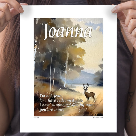 Female hands holding a personalised gift of an A4 poster in a watercolour style of a deer at the edge of forest featuring the name Joanna at the top and a Biblical scripture Isaiah 41 verse 1 to the bottom left